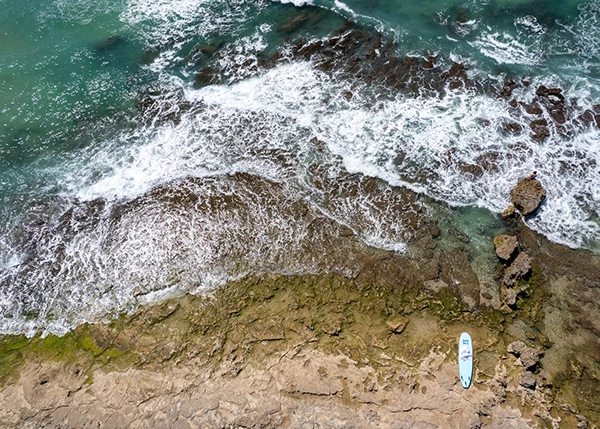 Breaking waves and a paddleboard near the rocky shore