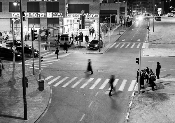 People crossing a lit intersection at night