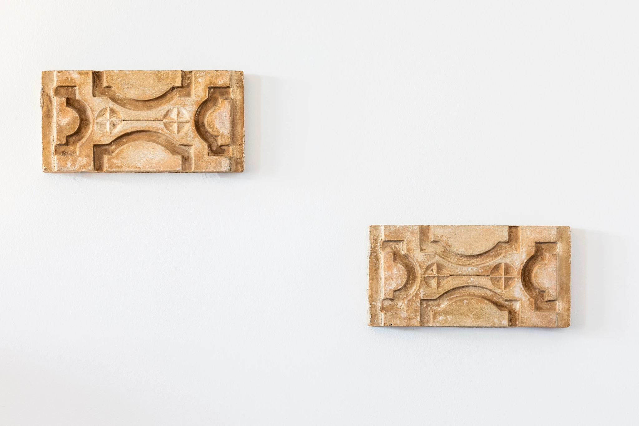 Two carved wall ornaments against a white wall