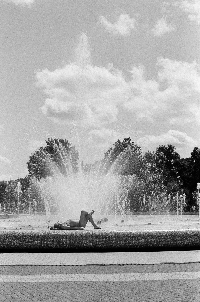 Black-and-white photograph of a fountain spraying water beneath clouds