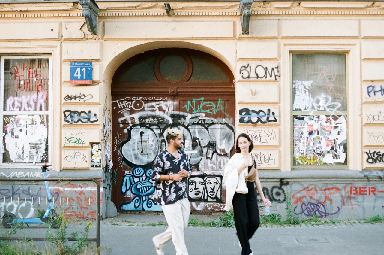 Two people walking in front of a graffiti-covered doorway